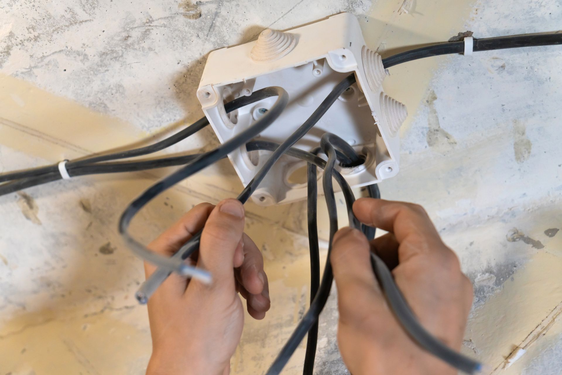 Hands holding electrical wires in a wall opening during wiring installation