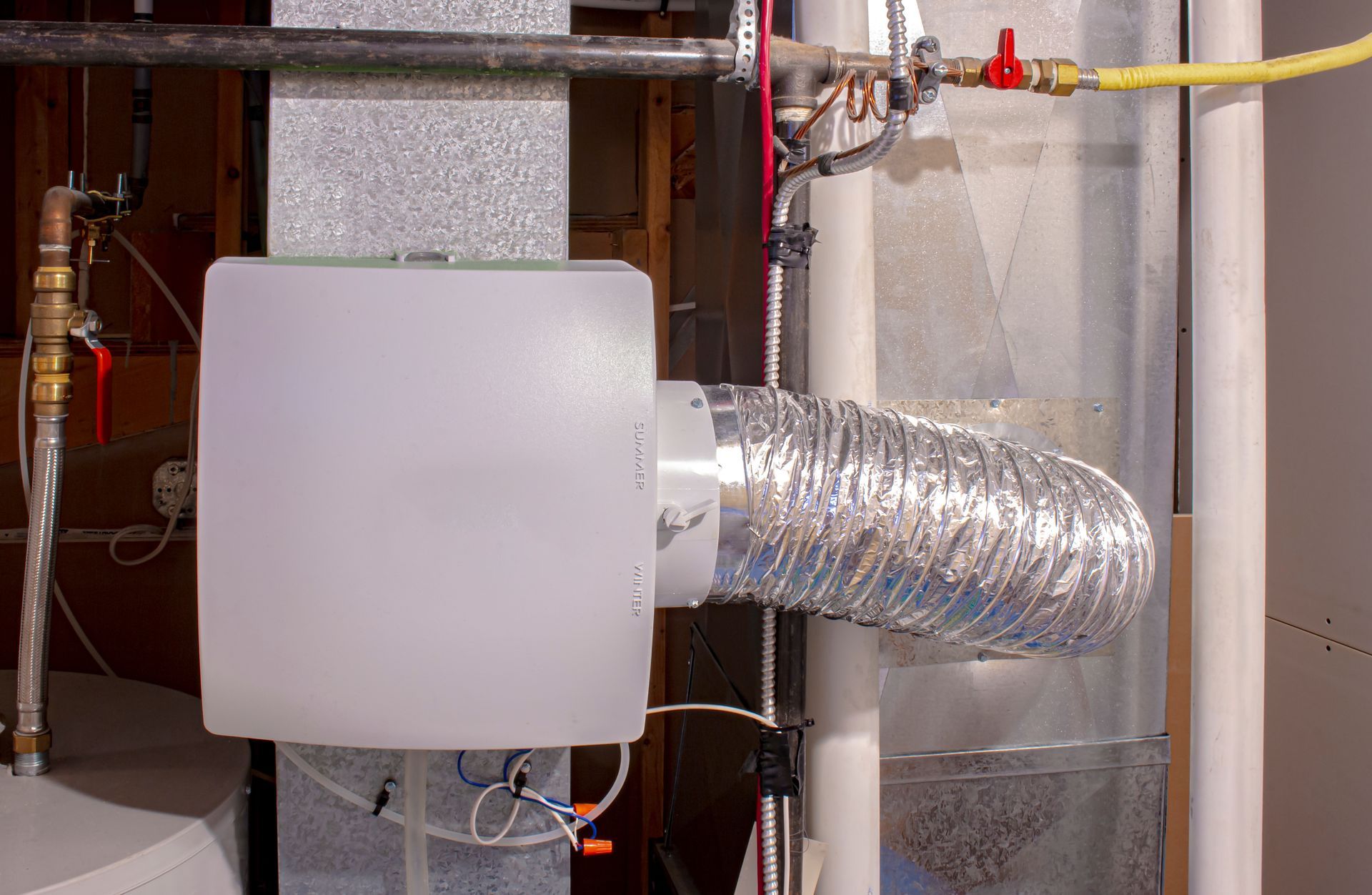 HVAC ventilation duct with silver flexible hose attached to a white wall-mounted unit in a utility room