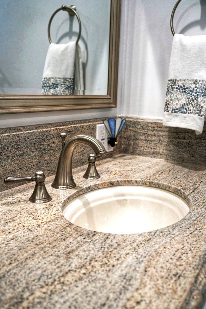 Bathroom vanity with granite countertop, oval sink, bronze faucet, mirror, and white towels