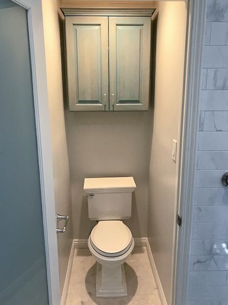 Small bathroom with a toilet centered below a wall cabinet, framed by a narrow doorway.