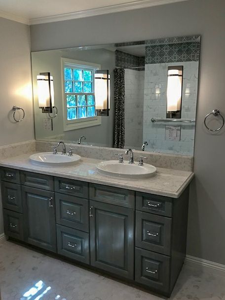 Bathroom vanity with double sinks, dark cabinets, large mirror, and tiled shower in the background