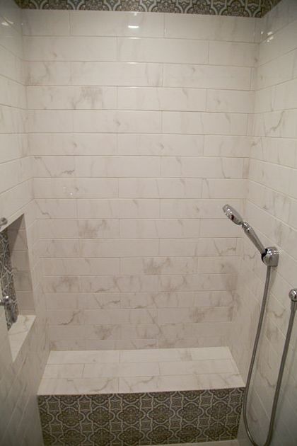 White tiled shower stall with built-in bench and handheld showerhead on the right.