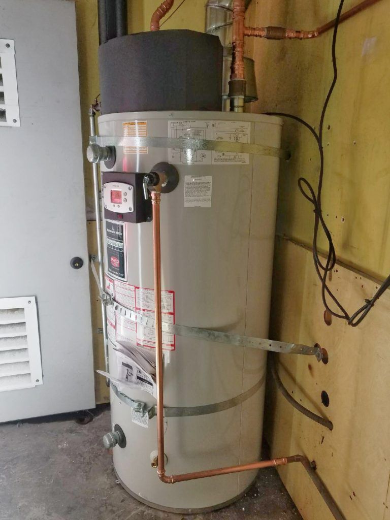 Water heater with copper pipes and labels in a utility room against a yellow wall.