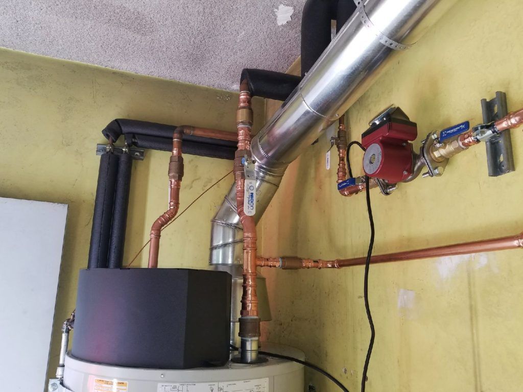 Industrial ceiling piping with insulated ducts, copper pipes, and a red pump on a yellow wall