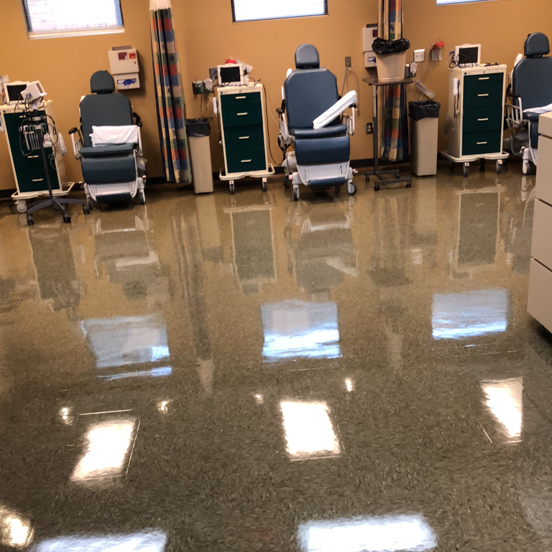 A brightly lit medical room with several chairs and medical equipment, reflecting light off a shiny floor.