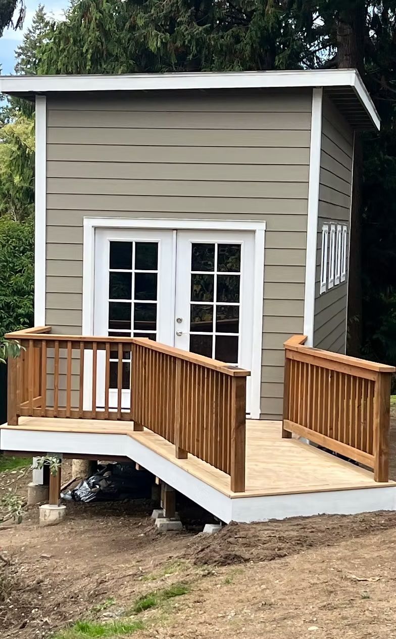 Small, elevated building with wooden deck and ramp. White double doors, tan siding, and brown railing.