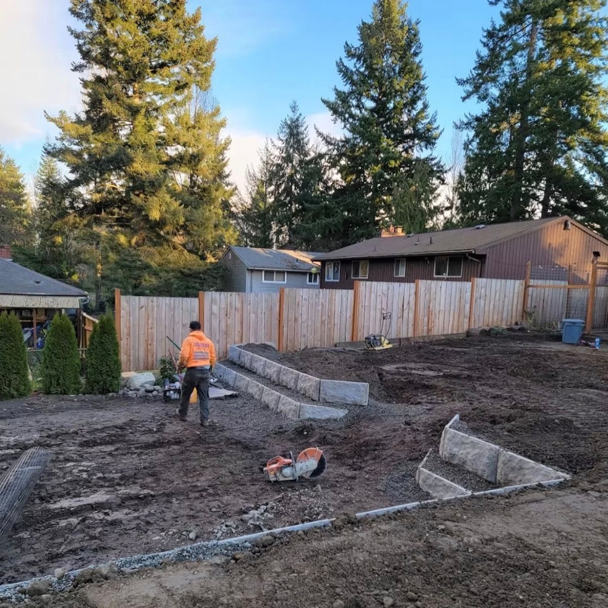 Backyard construction with a worker, raised beds, and new wooden fence.