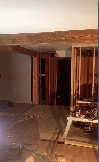 Interior room under construction, with exposed wooden beams, studs, and dark doorway in the distance.