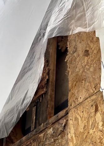 Damaged wood framing under a white tarp. The wood shows significant deterioration.