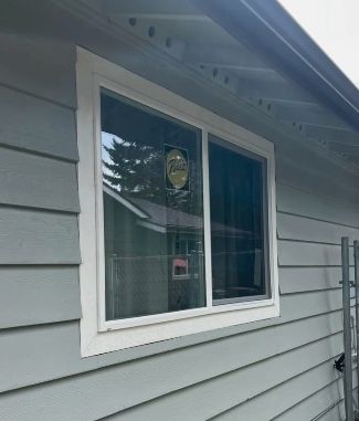 A newly installed window with white trim on a light gray siding house.