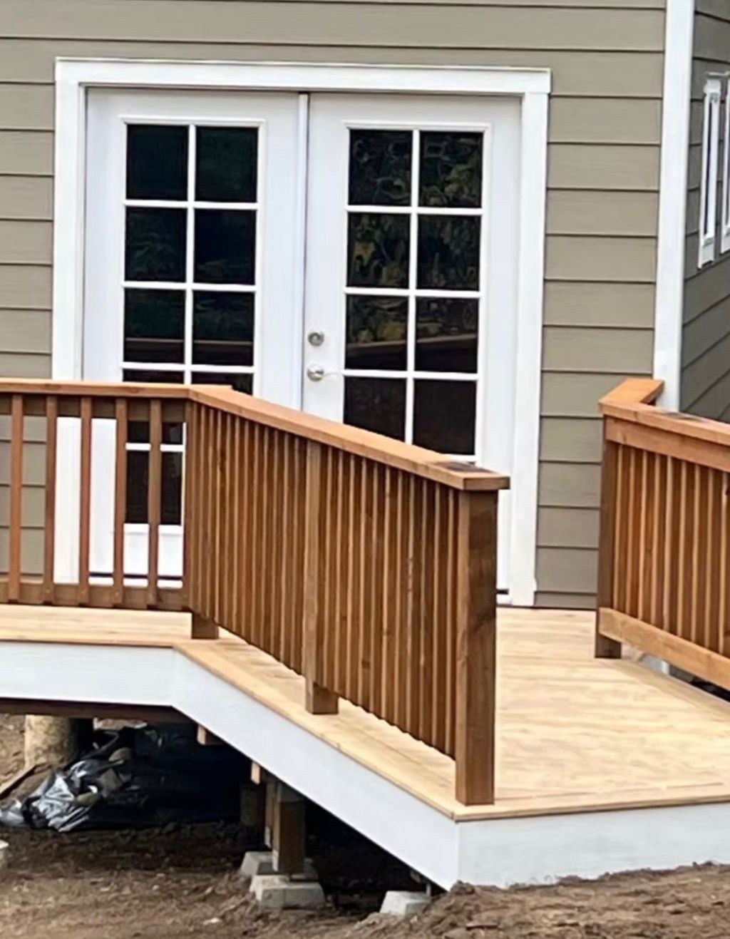 Wooden deck with ramp and handrail leading to white French doors on a building with green siding.