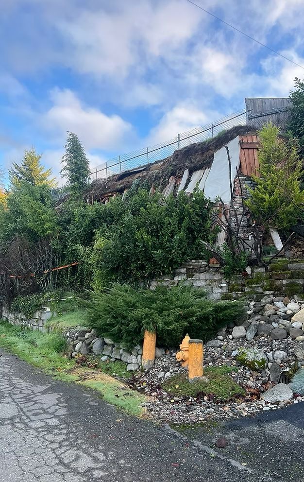 Damaged building on a hillside, partially collapsed. Yellow fire hydrants in the foreground, cloudy sky.