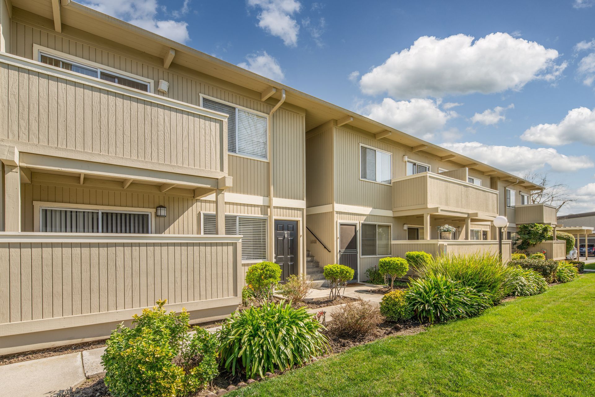 Townhomes with beige siding, balconies, and green landscaping under a blue sky.