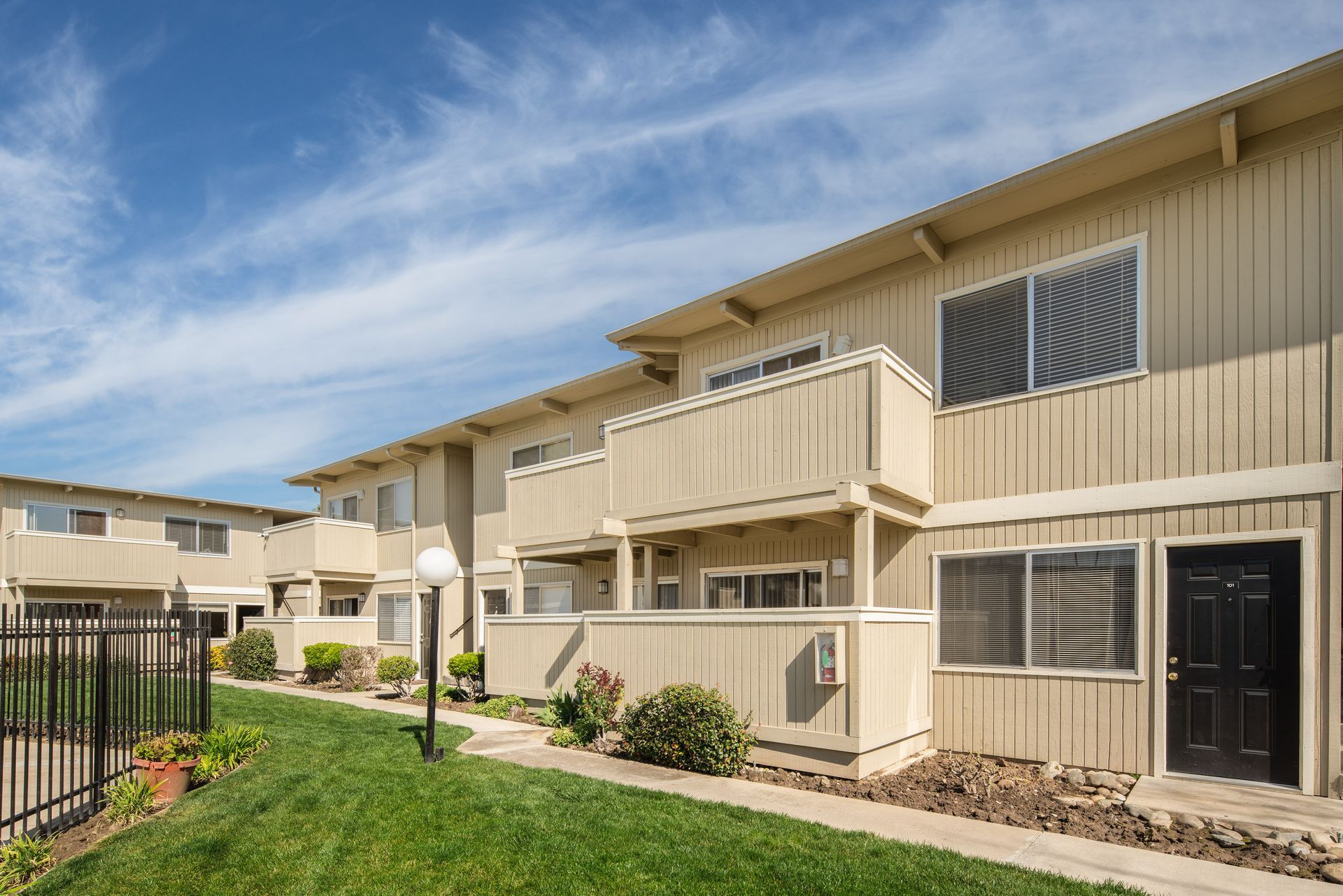 Apartment complex exterior with tan siding, balconies, and green lawn under a blue sky.