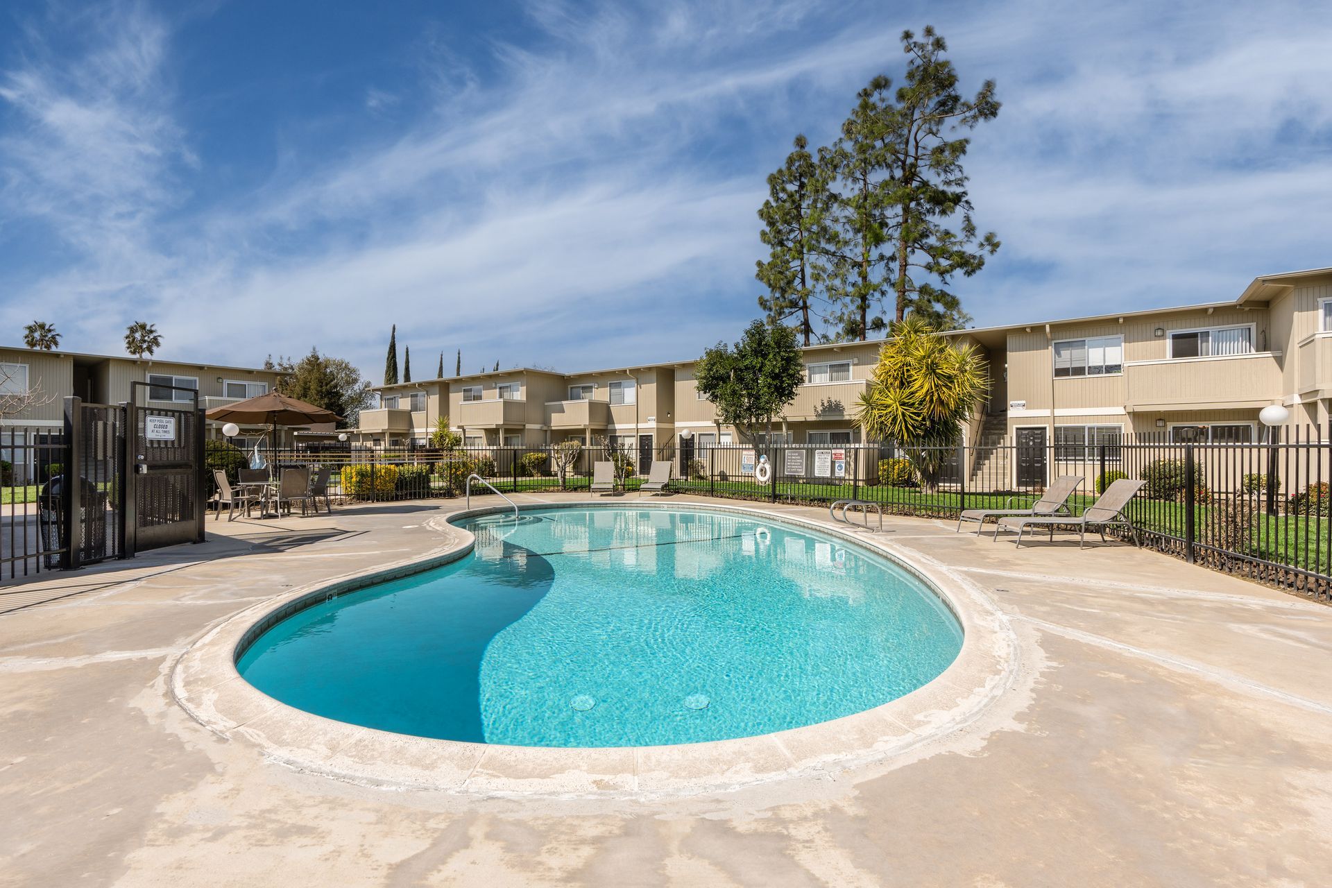 Pool in front of two-story apartment buildings under blue sky.