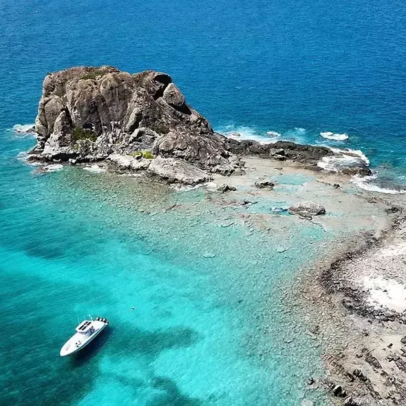 Island rock formation in turquoise water, with a small boat anchored nearby.