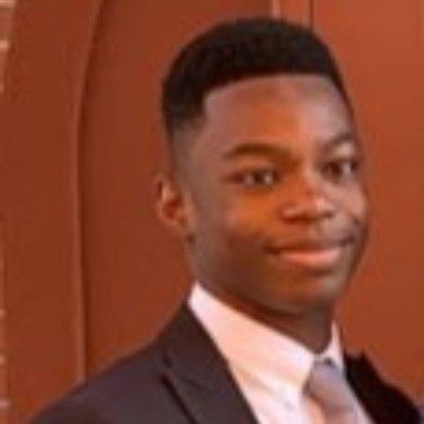 Young person in a dark suit and tie, smiling slightly against a warm brown background