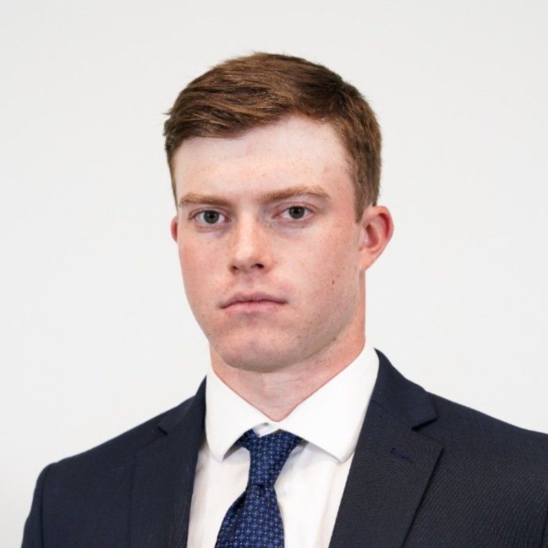 Portrait of a man in a dark suit, white shirt, and blue tie against a plain white background