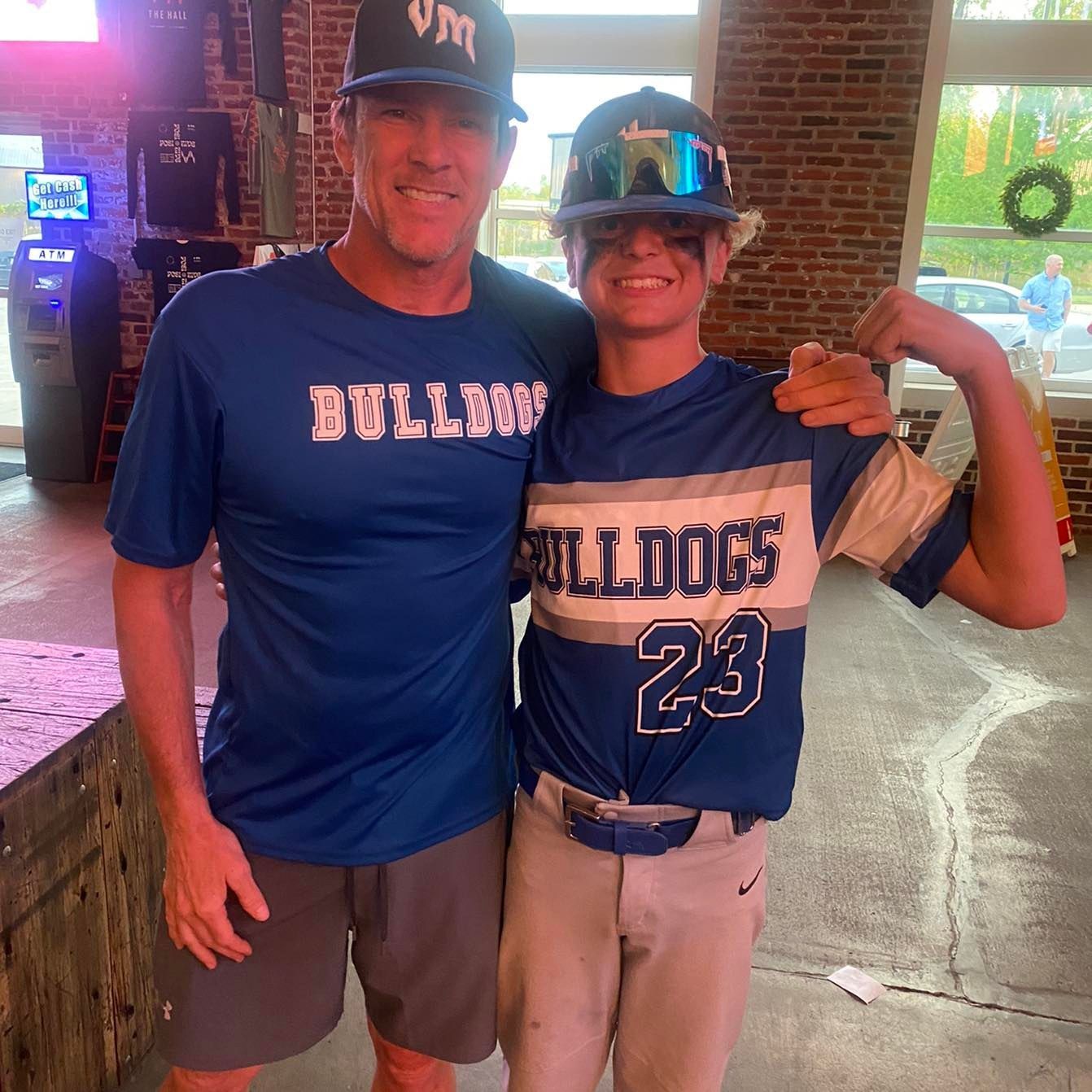 Two people in Bullys baseball shirts and caps pose together indoors, smiling and arm-in-arm.