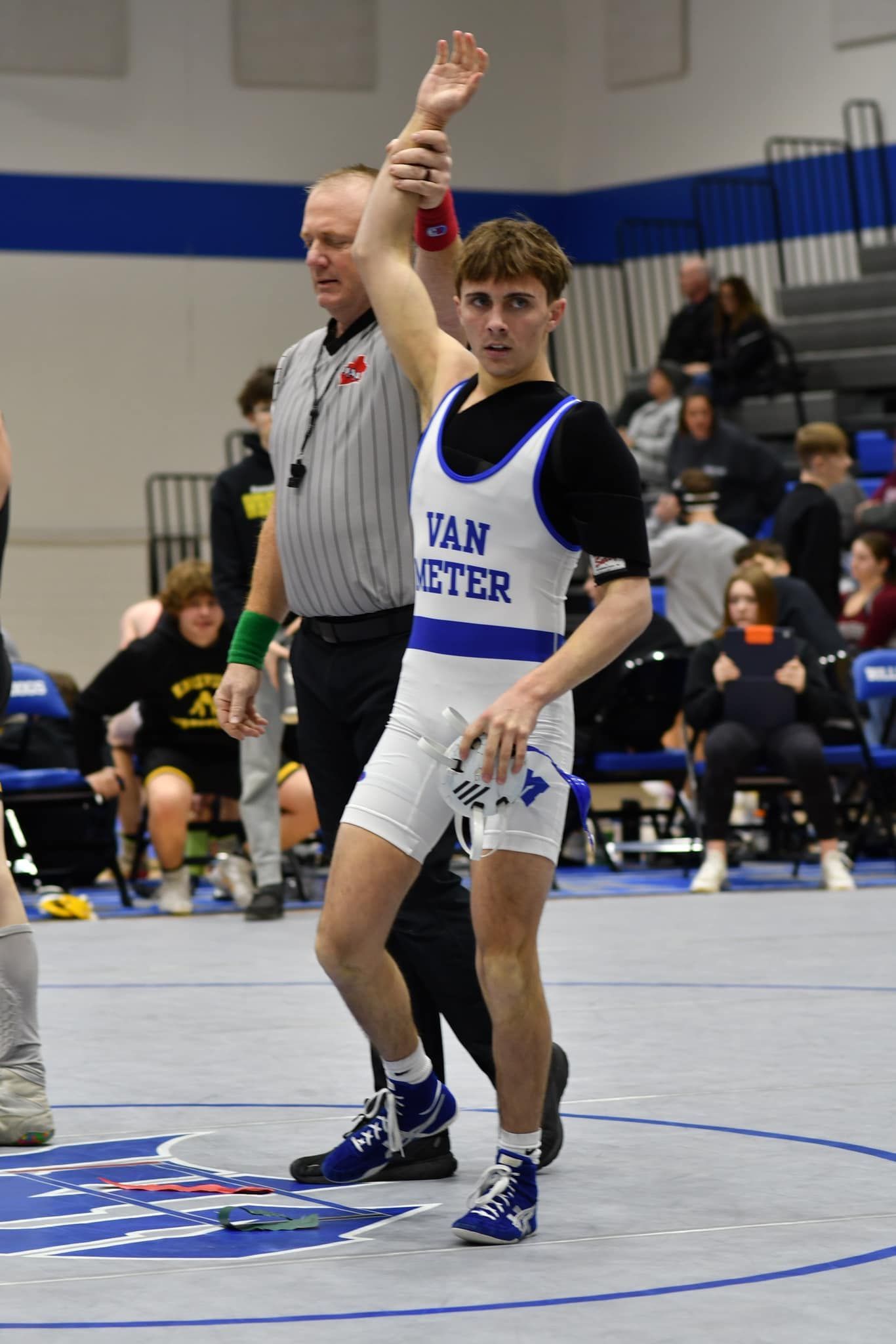 Wrestler in white and black singlet raises an arm on the mat during a gym match