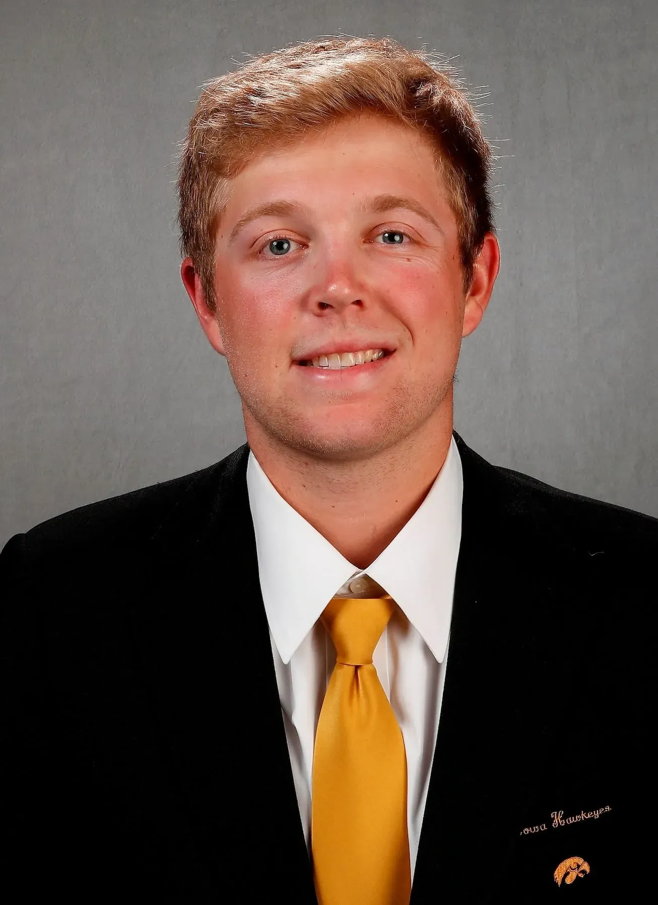 Portrait of a person in a black suit and gold tie against a gray studio background