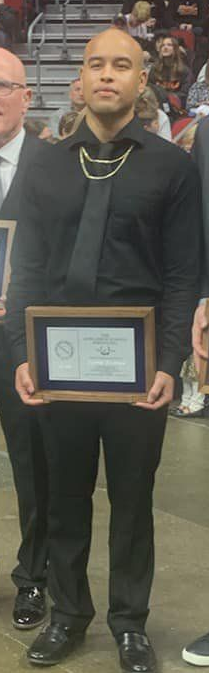Man in black clothing holding a framed certificate at an indoor event