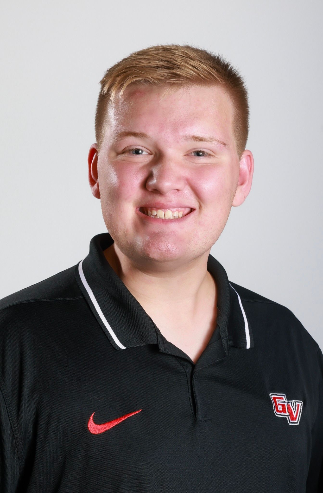 Person smiling in a black polo shirt with red logos against a gray background