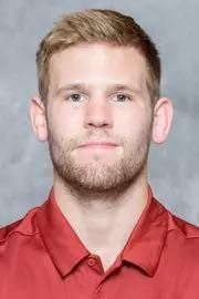 Head-and-shoulders portrait of a man in a red collared shirt against a gray background