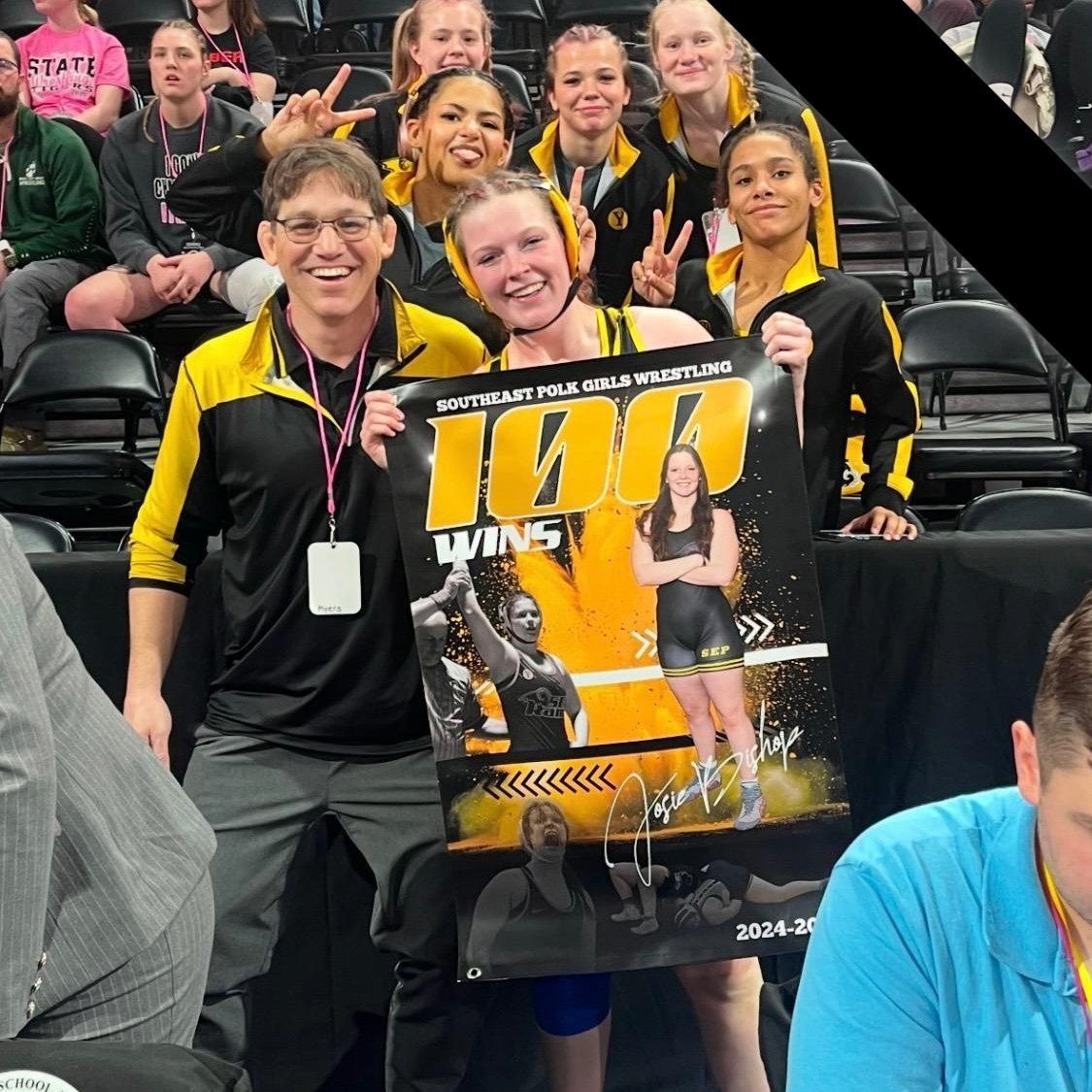Two women in black and yellow shirts hold a large 1000 poster in a stadium seating area.