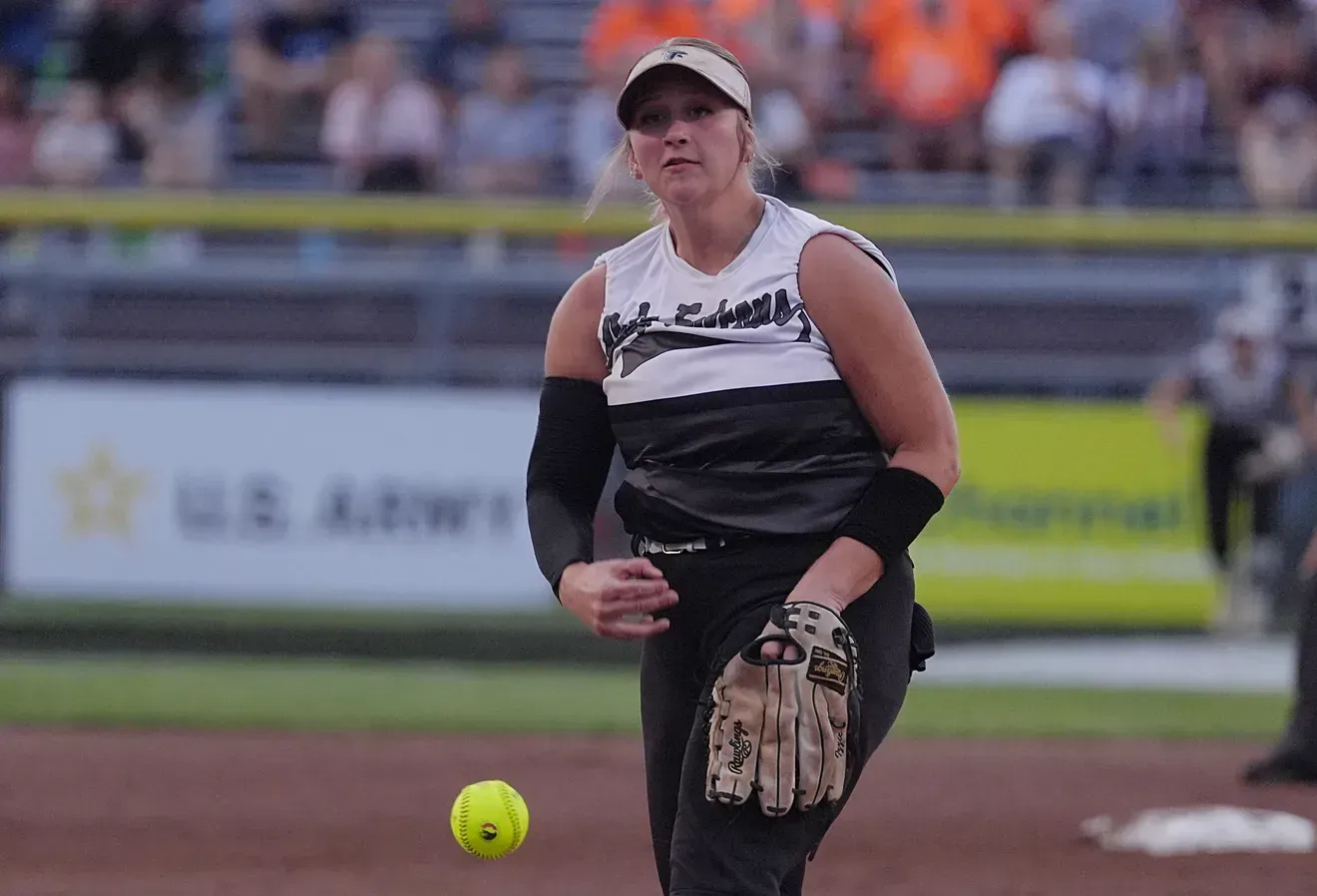 Softball player in black-and-white uniform fielding a ball on the infield during a game.