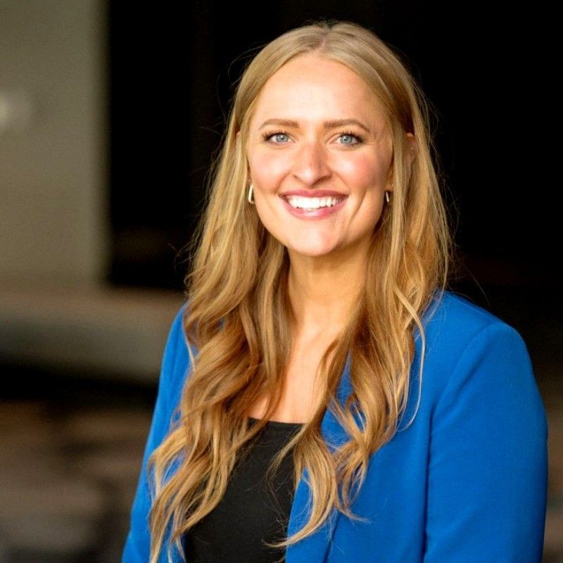 Smiling woman in a blue blazer and black top against a blurred indoor background