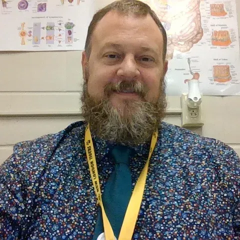 Smiling man in patterned shirt and tie in an office, with medical posters on the wall