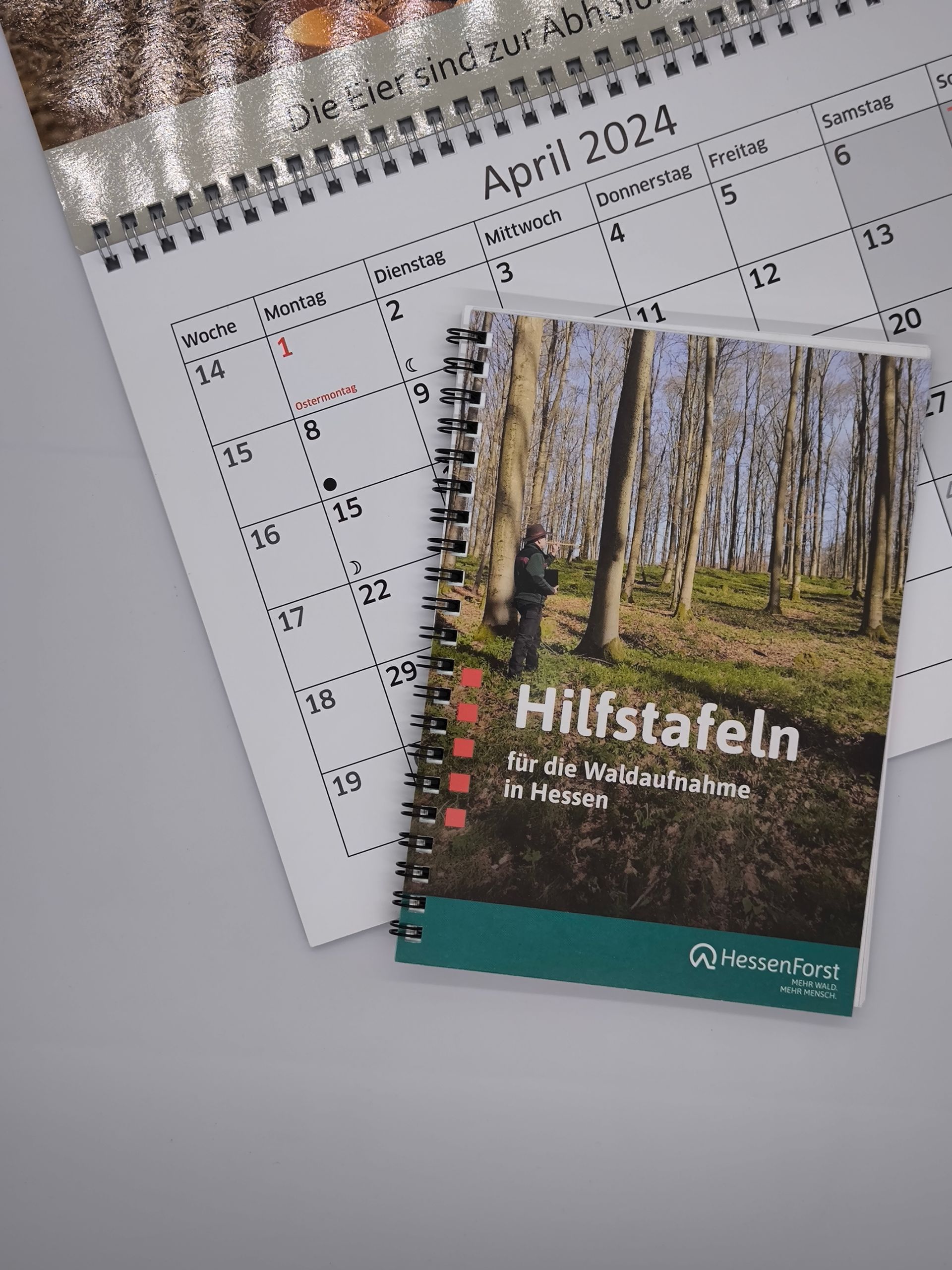 Ein spiralgebundenes Buch mit dem Titel „Hilfstafeln“ liegt neben einem Kalender