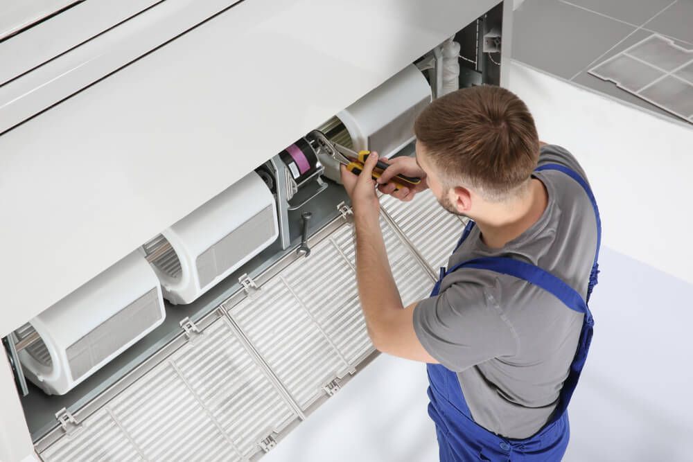 A Technician Servicing an Air Conditioner in a Room — Air Conditioning Near Me in the Whitsundays Region