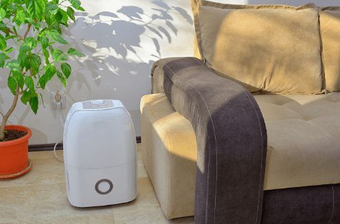 A Dehumidifier is Sitting Next to a Couch in a Living Room — Refrigerated Technologies (QLD) Pty Ltd In Collinsville, QLD