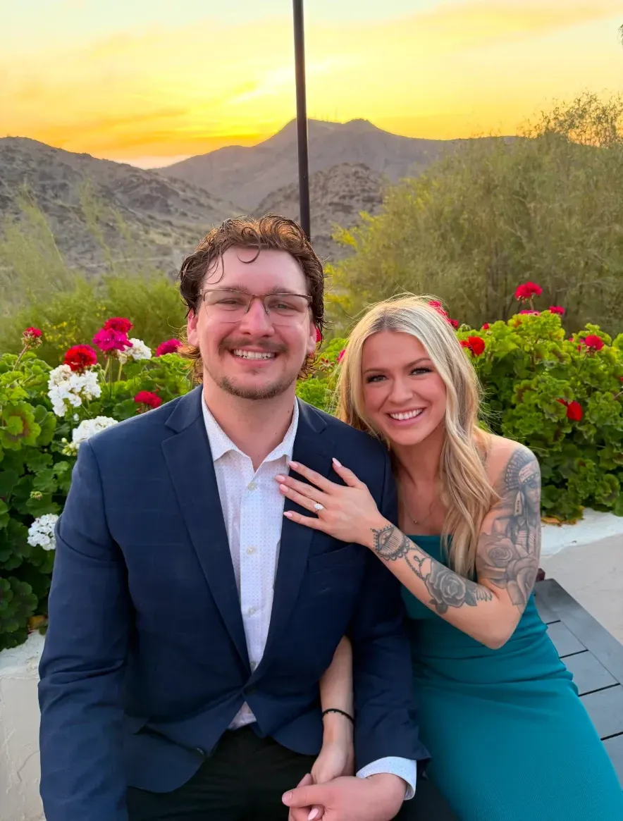 A man and a woman are posing for a picture in front of a mountain.
