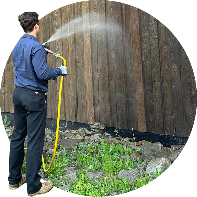 A man spraying a wooden wall with a hose