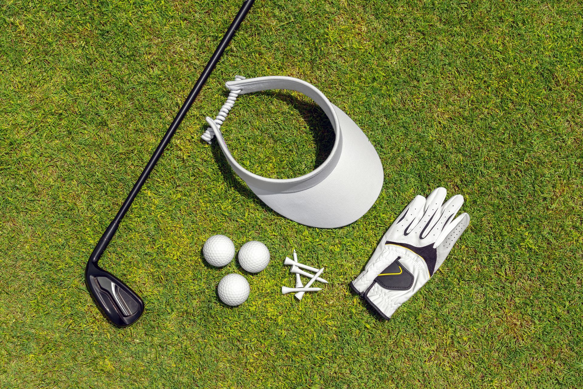 Golf club, visor, glove, tees, and golf balls arranged neatly on a green practice surface.