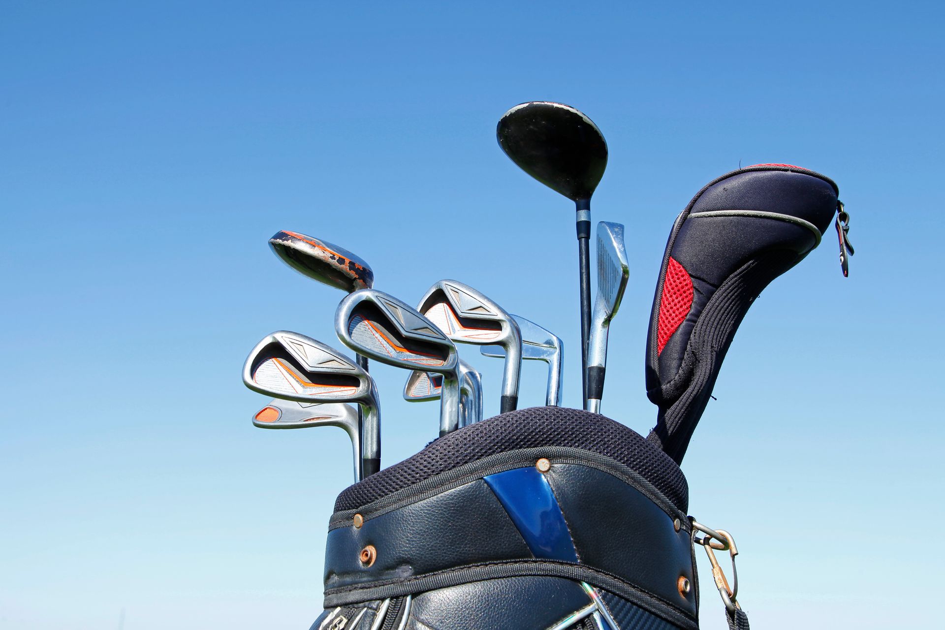 Golf bag filled with clubs and headcovers positioned outdoors against a clear blue sky.
