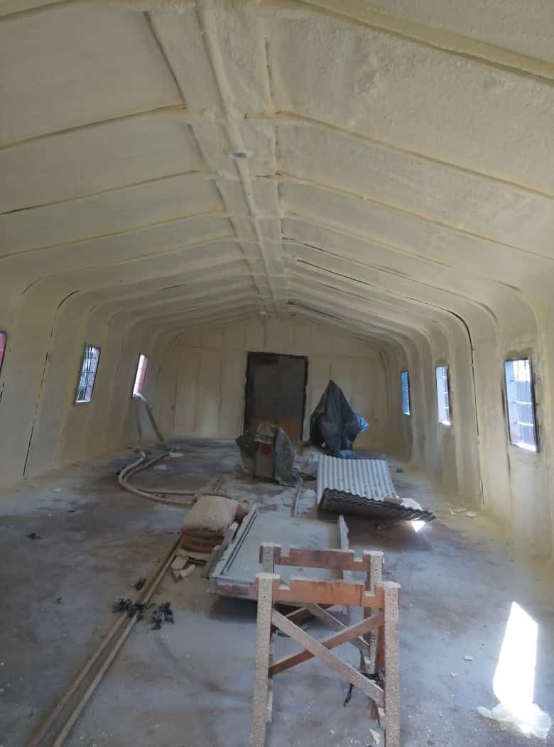 Vista interior de un edificio con aislamiento de espuma en aerosol en paredes y techo. Escombros de construcción esparcidos.