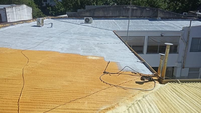 Un tejado con aislamiento de espuma, parcialmente aplicado en color naranja, junto a una sección terminada en gris claro.