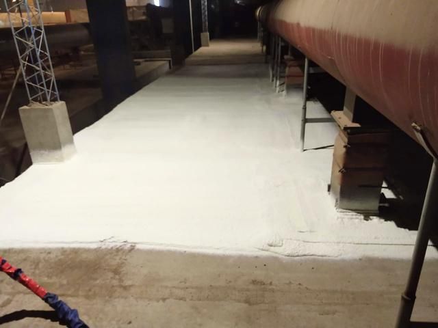 Una pasarela blanca bajo una tubería roja, iluminada por luces de techo durante la noche.