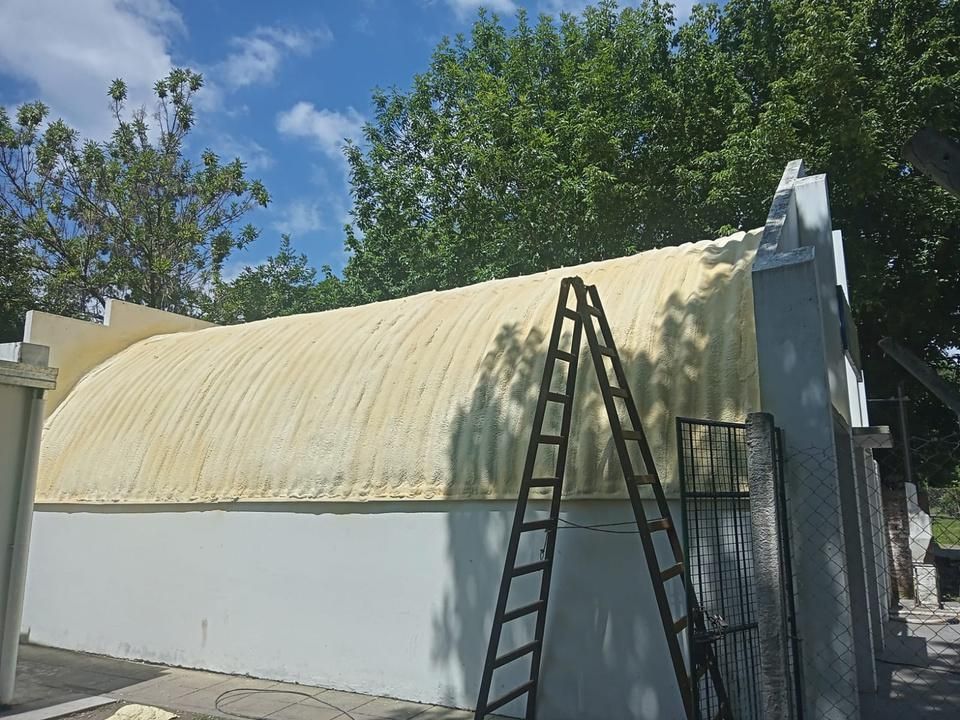 Edificio blanco con techo arqueado recubierto de aislamiento de espuma amarilla; una escalera se apoya en él.
