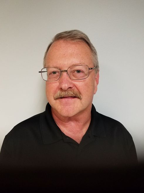 Portrait of a man with glasses and a mustache, wearing a black shirt against a plain light background