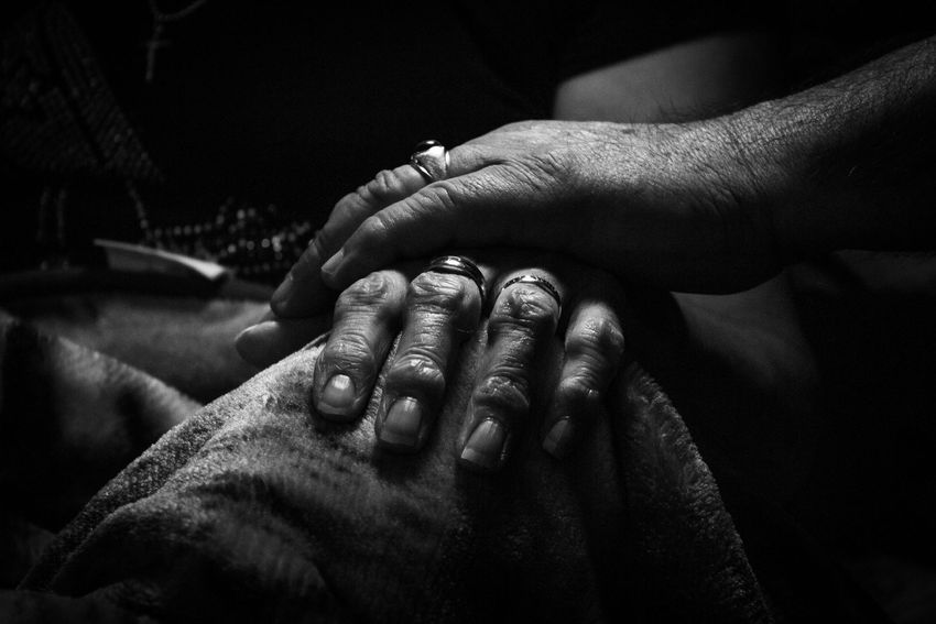 Two hands gently resting on a person’s back in a dim black-and-white setting.