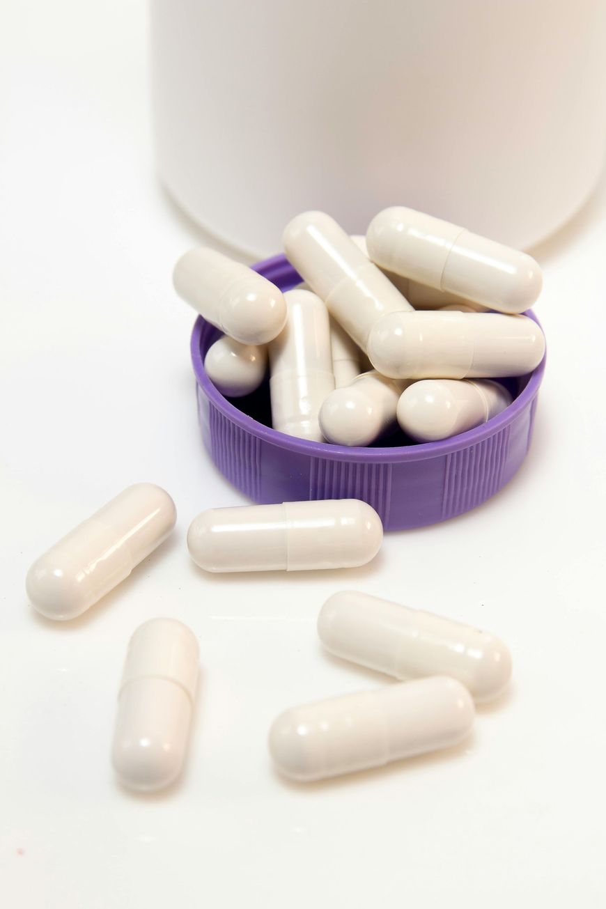 White capsules spilling from a purple bottle cap on a white surface