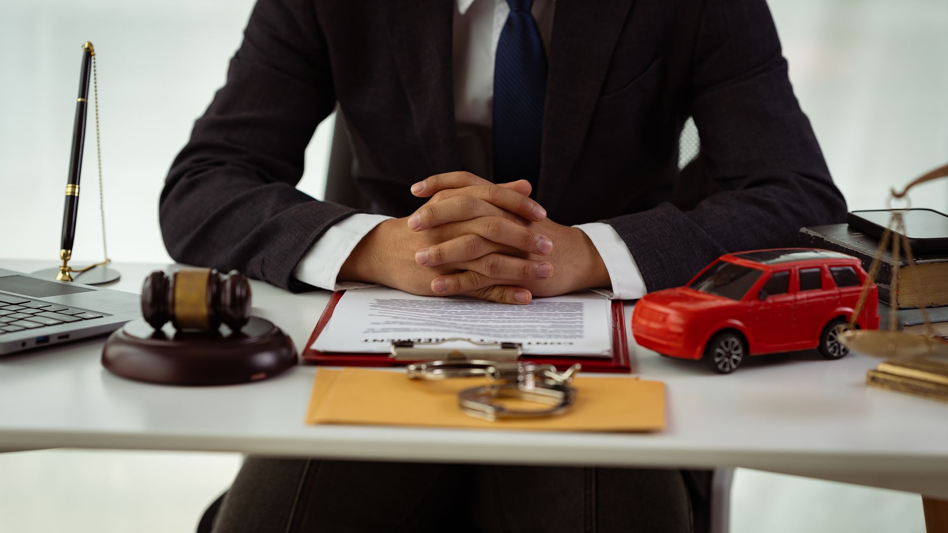 A man in a suit and tie is sitting at a desk with a red car and a judge 's gavel.