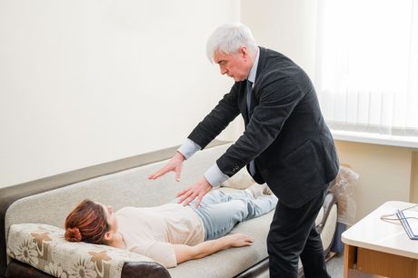 Man performing a therapy session on a woman lying on a couch. The man is holding his hands above the woman.
