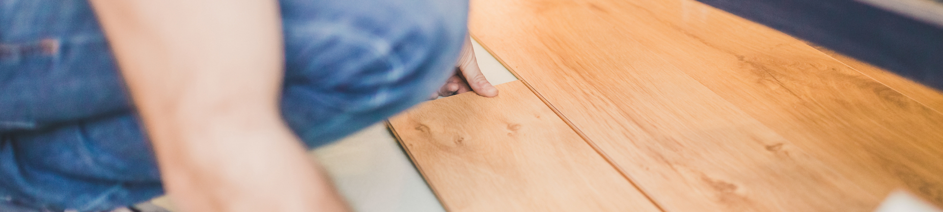A person in blue jeans kneeling on the floor to install wooden laminate planks.