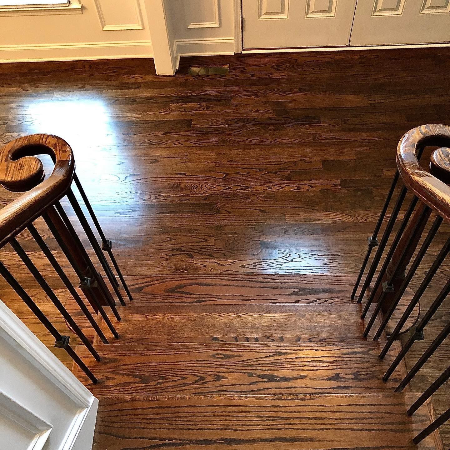 Top-down view of dark hardwood floor between two stair railings leading to a kitchen area.